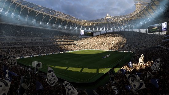 Een voetbalstadion met het Tottenham Hotspur-logo, de tribunes vol fans, de zon schijnt op het veld.