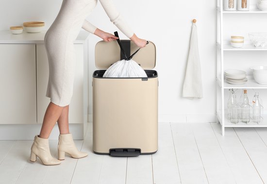 Une femme en robe en tricot retire un sac poubelle de la poubelle Brabantia Bo crème.
