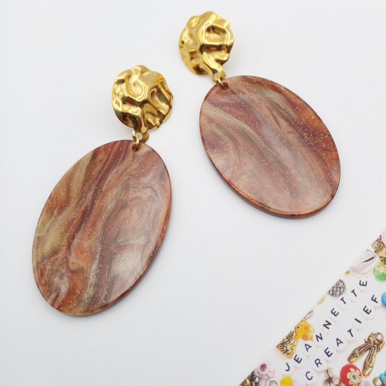 Gouden oorknopjes met bruine, ovale harsdruppels met glittereffect.