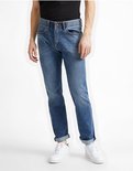 Man in een lichtblauwe jeans met opgerolde broekspijpen, gedragen met witte sneakers.