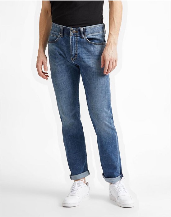 Man in een lichtblauwe jeans met opgerolde broekspijpen, gedragen met witte sneakers.
