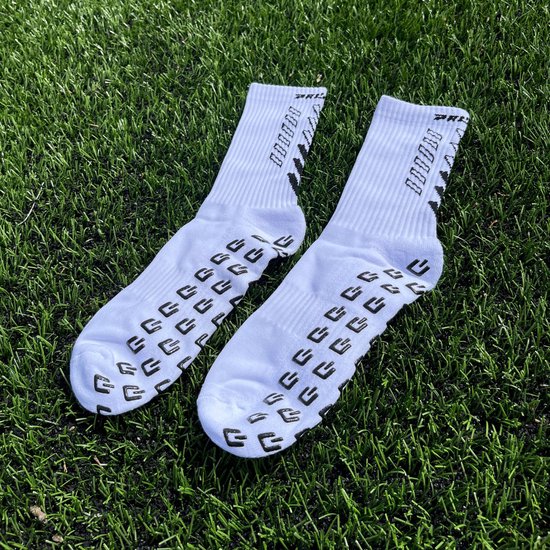 Une paire de chaussettes blanches avec des éléments de grip noirs et des logos sur du gazon artificiel.