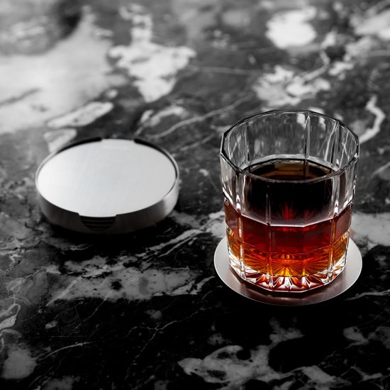 Glazen whisky met amberkleurige drank op een ronde RVS onderzetter. Naast een gesloten RVS onderzetterhouder.