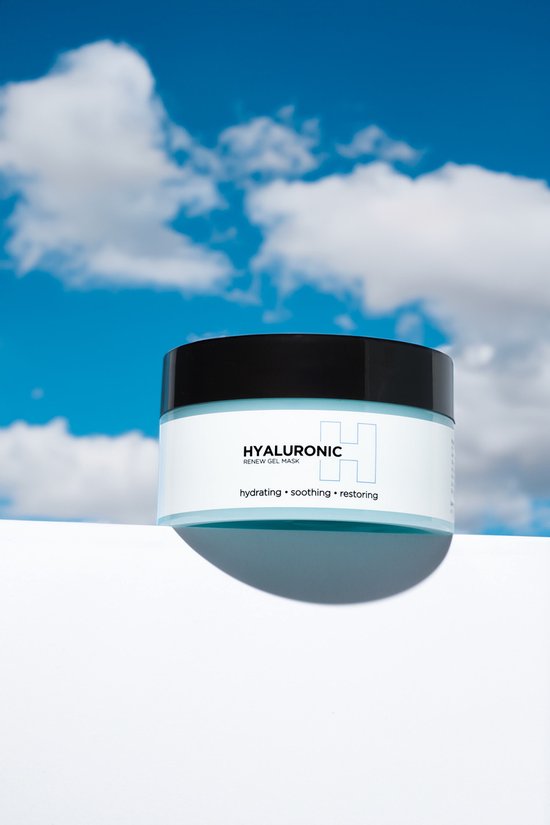 Glazen pot met lichtblauw hyaluronzuur masker op een witte kubus onder een blauwe hemel met wolken.