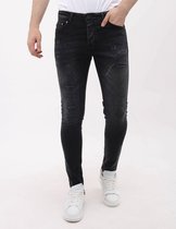 Model in donkergrijze slim fit jeans met scheuren en witte sneakers.