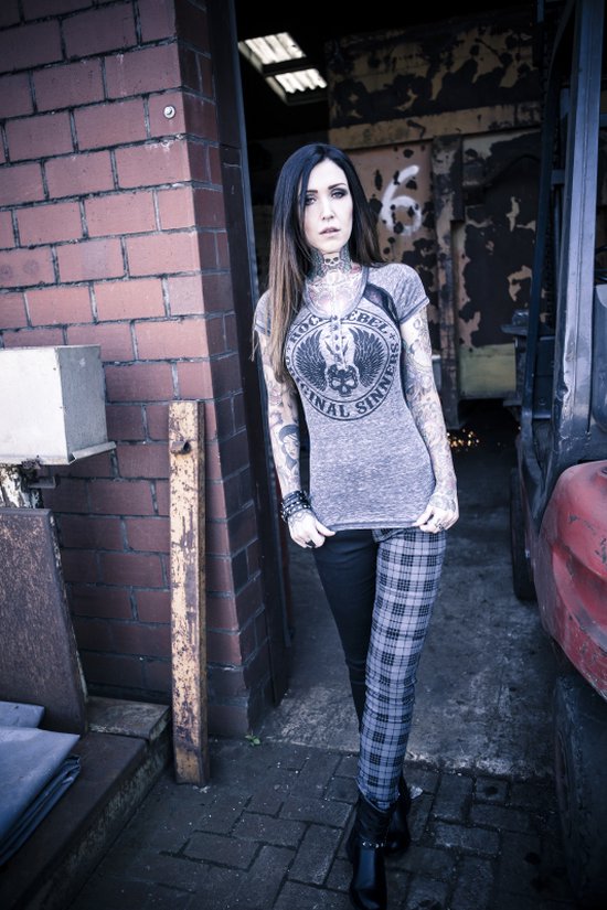 Model met lang, donker haar, draagt een grijs t-shirt met opdruk en een broek met aan de linkerzijde een grijze ruit en aan de rechterzijde zwart. Zwarte enkellaarsjes.