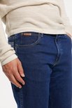 Dichtbij opname van een spijkerblauwe Wrangler spijkerbroek met bruine naden en een bruin leren label op de zak.