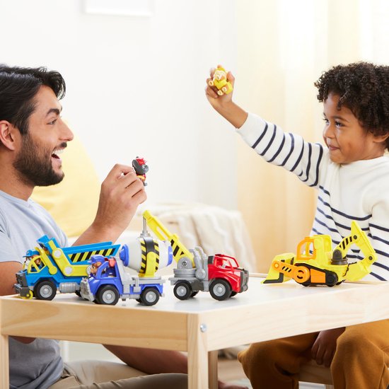 Man en jongen spelen met bouwvoertuigen, waaronder een blauwe kiepwagen.
