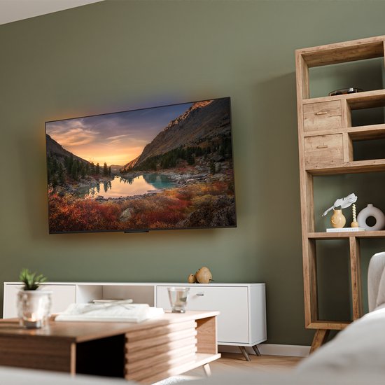 Een platte zwarte TV-beugel aan een groene muur, met een televisie erop die een berglandschap toont.