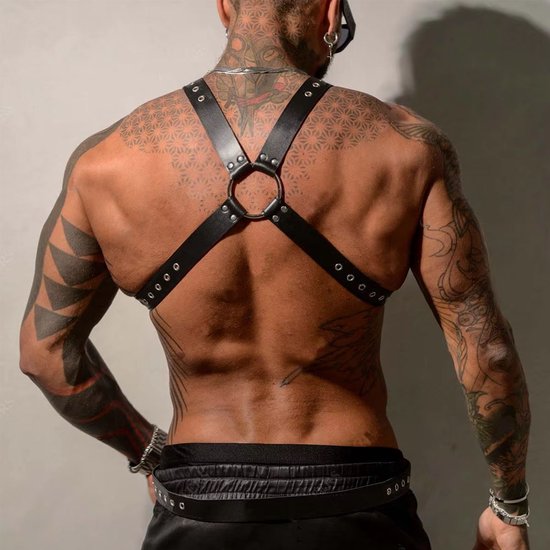 Achteraanzicht man met zwart kunstleren harnas, tattoos op rug en armen.
