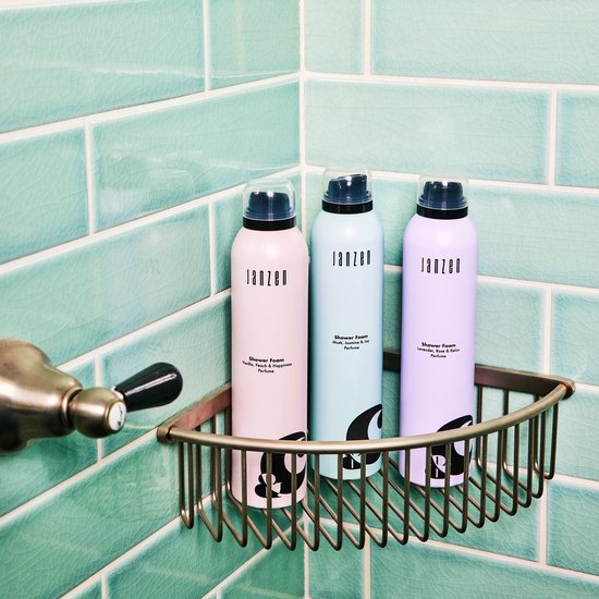 Roze, lichtblauwe en paarse spuitbussen Janzen Shower Foam in een douchehoek op een messing rekje.