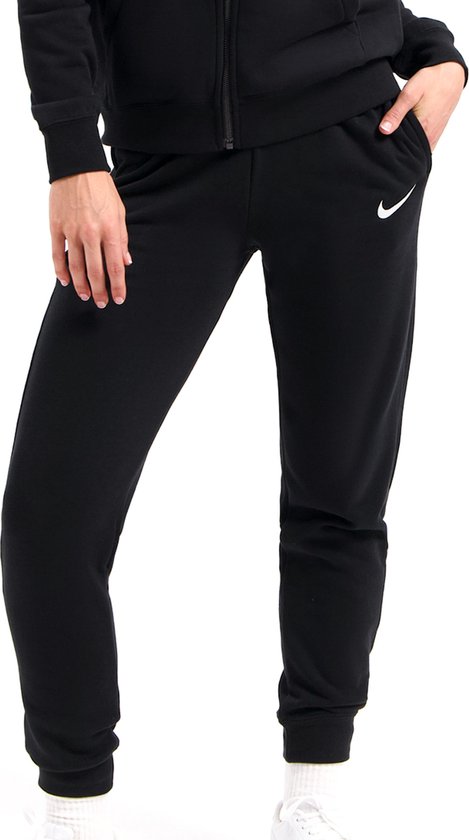 Model draagt een zwarte Nike trainingsbroek met witte sportsokken en sneakers. Broek heeft een logo op de heup.