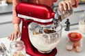Vrouw voegt chocoladedruppels toe aan rode KitchenAid Artisan keukenmachine.