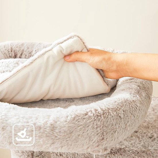 Een hand legt een zacht, wit kussen in een pluche mand van een kattenboom.