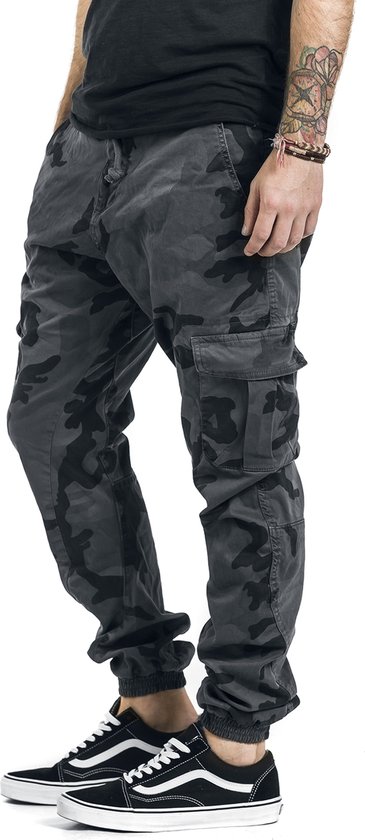 Man met camouflage cargo broek met cargo zakken, zwart T-shirt en Vans sneakers.