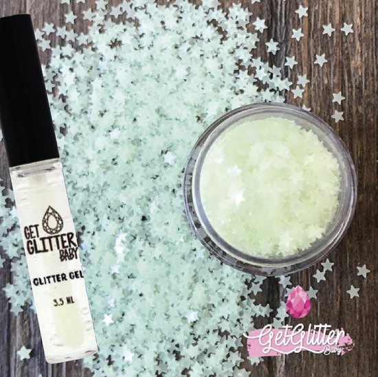 Een tube glittergel en een potje met lichtgroene sterglitters verspreid op een houten ondergrond.
