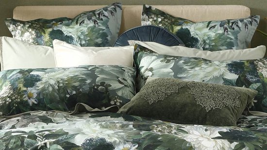 Lit décoré avec de nombreux coussins à imprimé floral vert et blanc. Un coussin en velours vert avec broderie.