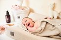 Lachende baby ingepakt in een beige handdoek op een beige Jollein aankleedkussen.
