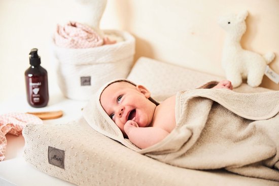 Lachende baby ingepakt in een beige handdoek op een beige Jollein aankleedkussen.