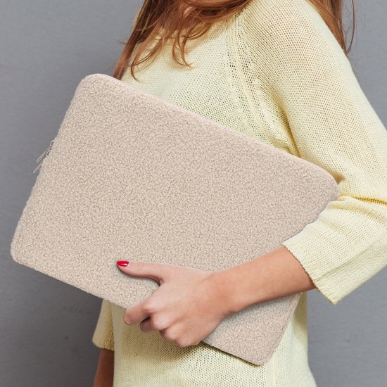 Une femme portant un pull jaune tient une housse d'ordinateur portable en tissu pelucheux beige.