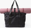 Sac fourre-tout noir avec un tapis de yoga rose enroulé sur le dessus.