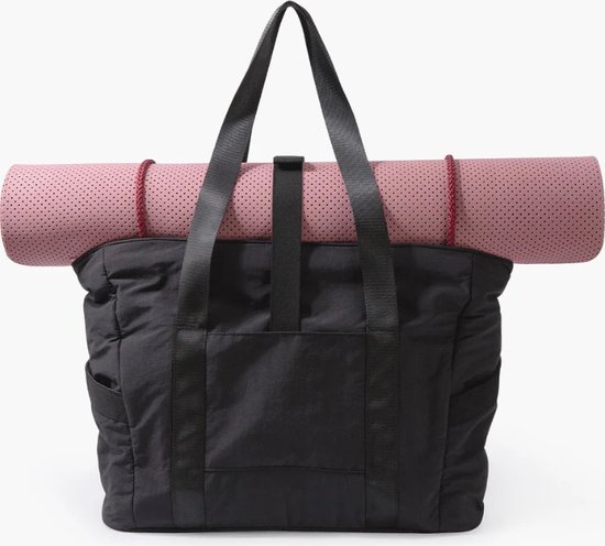Sac fourre-tout noir avec un tapis de yoga rose enroulé sur le dessus.