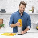 Man in blauw denim shirt maakt een oranje smoothie in een linnen beige Nutribullet.