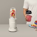 Linnen beige Nutribullet met een beker vol vijgen, aardbeien, perziken, walnoten en ijs, naast een man met smoothie.