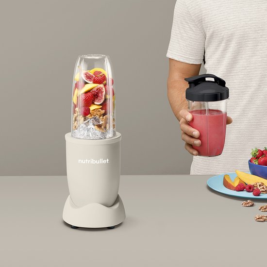 Linnen beige Nutribullet met een beker vol vijgen, aardbeien, perziken, walnoten en ijs, naast een man met smoothie.