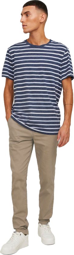 Man met gestreept blauw-wit T-shirt en beige chino broek, staand met handen in de zakken.