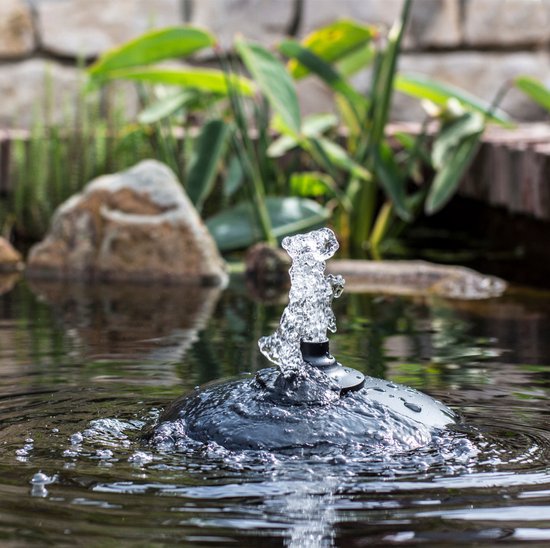 Zwarte fontein met waterstraal in een vijver. Op de achtergrond groen blad en stenen.