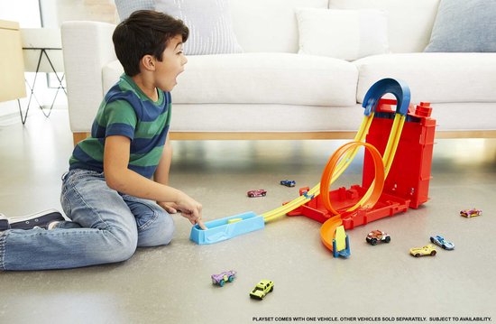 Un garçon surpris est à genoux et regarde le set Hot Wheels Track Builder avec des pistes rouges, jaunes et oranges.