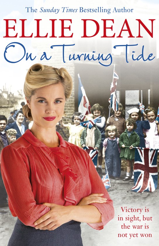 Boekcover van 'On a Turning Tide' door Ellie Dean. Een vrouw in een rode blouse met opgestoken haar, met kinderen en vlaggen op de achtergrond.