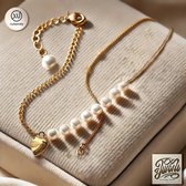 Gouden ketting met parels en hartvormige bedel op een beige achtergrond.