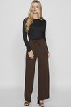 Vrouw met lange blonde haren, draagt bruine wijde broek.