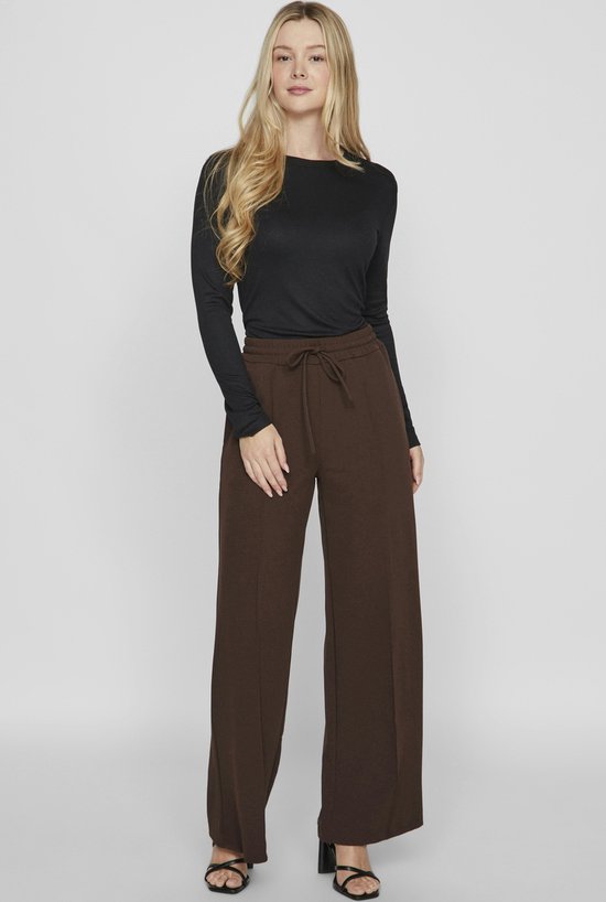 Vrouw met lange blonde haren, draagt bruine wijde broek.