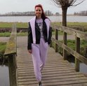 Vrouw met rood haar draagt een zwarte leren jas en een paarse joggingbroek.
