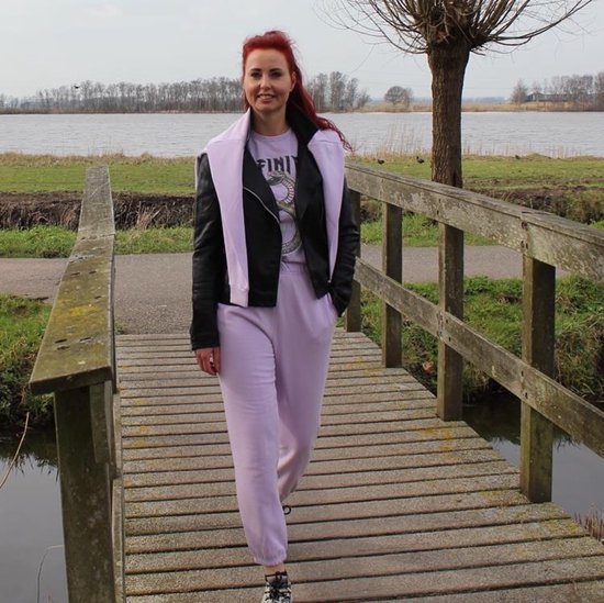 Vrouw met rood haar draagt een zwarte leren jas en een paarse joggingbroek.