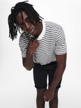 Man met dreadlocks draagt gestreepte t-shirt en zwarte shorts.
