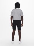 Man met gestreept t-shirt en zwarte denim shorts, witte sneakers, gezien van achteren.