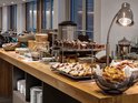 Een buffet met diverse taarten, brood, croissants en een warme drankdispenser.