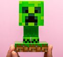 Een Minecraft Creeper figuur op een groen gras- en aardeplatform, vastgehouden in handen.