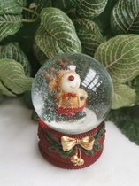 sneeuwbol met feestelijk geklede eland  en  kerstboom op prachtig versierde rode sokkel