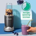 Nutribullet blender met blauwe bessen en havermout, naast een glas met paarse smoothie.