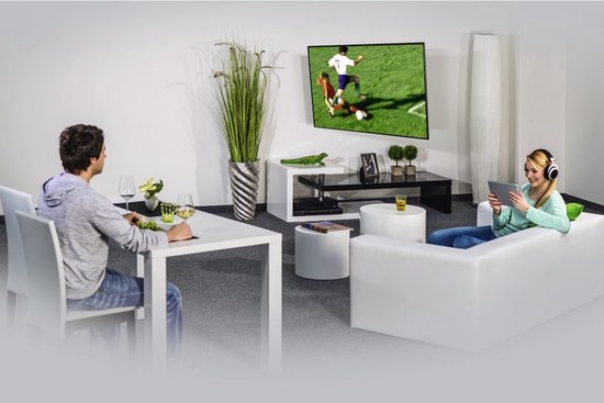Woonkamer met man die krant leest en vrouw op tablet, tv aan muur met voetbalwedstrijd.