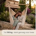 Stuk over elkaar in een crèmekleurige hangstoel, aan de rand van een bos.
