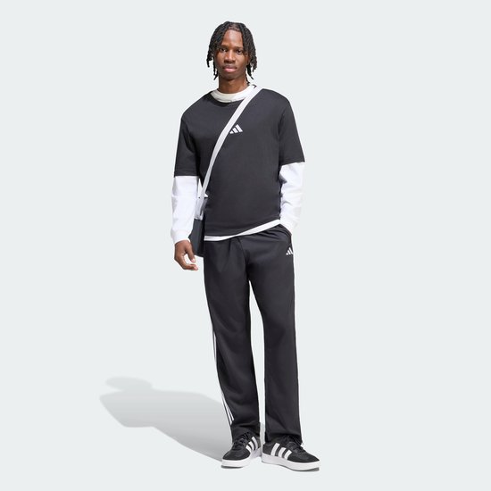 Man die een zwarte sportbroek met witte Adidas strepen draagt. Broek heeft een Adidas logo.