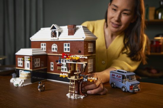 LEGO huis met sneeuw, kerstboom, figuur en bezorgbusje. Een LEGO figuur hangt aan een kabel.