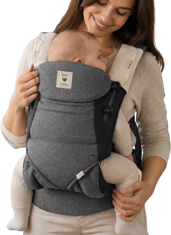 Een vrouw draagt een baby in een grijze draagzak met 'Born Lucky' label op witte achtergrond.