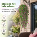 Hangplant met roze bloemen en groene bladeren, buiten aan een bakstenen muur. Tekst: 'Bloeiend het hele seizoen'.